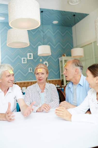 Group of senior friends with notepapers on foreheads playing name game at leisure - Photo, Image