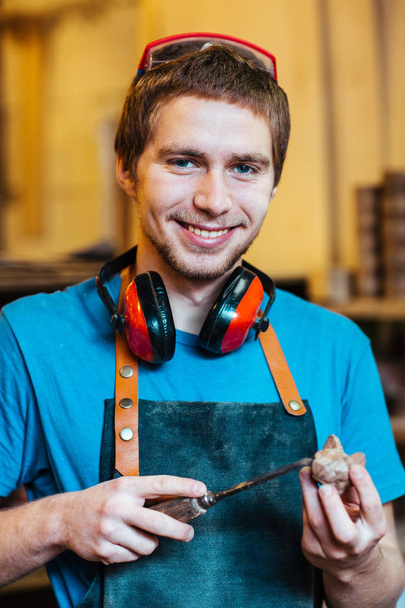 Porträt eines jungen Tischlers, der fröhlich in die Kamera lächelt und Holzspielzeug herstellt - Foto, Bild