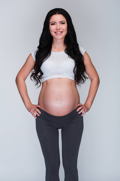 Casual güzellik. Güzel genç hamile kadın gülümseme duran, beyaz arka plan ile kameraya bakıyor - Fotoğraf, Görsel