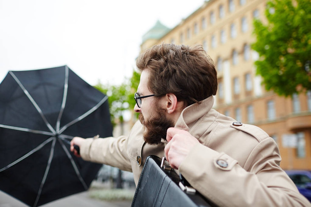 Бизнесмен с зонтиком противостоящий ветру во время работы
 - Фото, изображение
