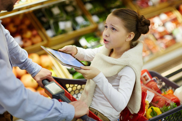 Menina insatisfeita com touchpad conversando com seu pai no supermercado
 - Foto, Imagem