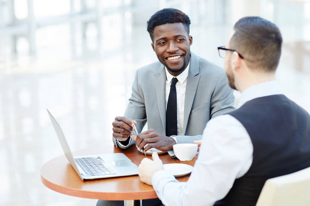 Retrato del exitoso hombre de negocios afroamericano sonriendo mientras discutía el trato con su pareja durante la reunión en el coffee break
 - Foto, Imagen