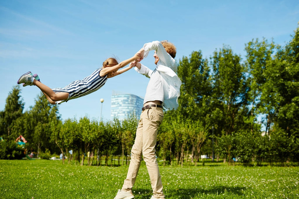 Jeune père tourbillonnant petite fille sur la pelouse verte tout en se reposant dans le parc
 - Photo, image