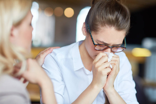 Young blond-haired woman comforting her upset best friend, she wiping nose with handkerchief, blurred background - Photo, Image