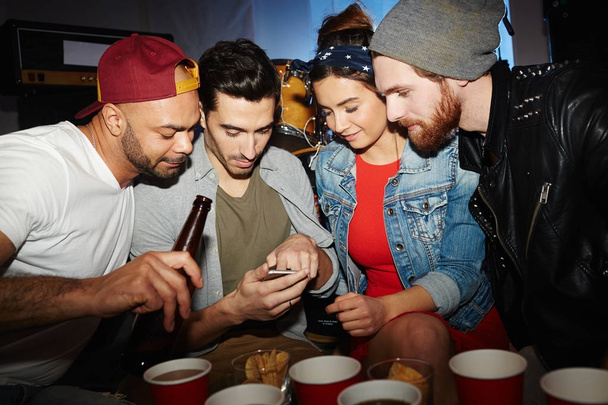 Grupo de amigos saindo na festa, olhando para a tela do smartphone do homem mostrando algo
 - Foto, Imagem