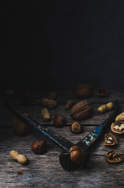 Various nuts, peanuts, hazelnuts and walnuts on old wooden table with tongs - Foto, afbeelding