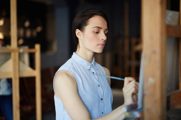 Caucasian girl painting on easel in art-school - Фото, изображение