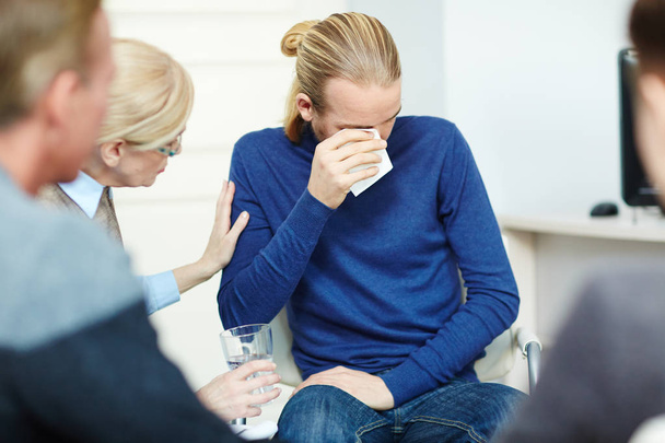 Portrait of young man sitting in circle of psychological support group crying while sharing his trouble with mentor and other participants - Photo, Image