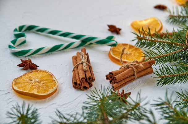 Candy cones with spices - anise stars, dried oranges, cinnamon sticks on the white background. Sweet Christmas heart of green candies on blurred background. New year food decorations with Christmas tree branch. Close up view - Photo, Image