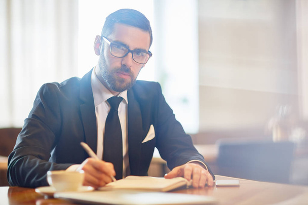 Young confident employer in suit making notes in notebook while planning working day - Photo, Image