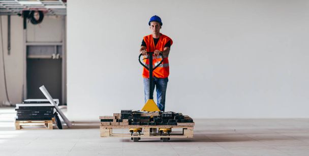 Handmatige werknemer rijden bouwmateriaal met hand pallettruck - Foto, afbeelding