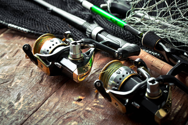 Fishing rods and spinnings in the composition with accessories for fishing on the old background on the table - Foto, Imagen