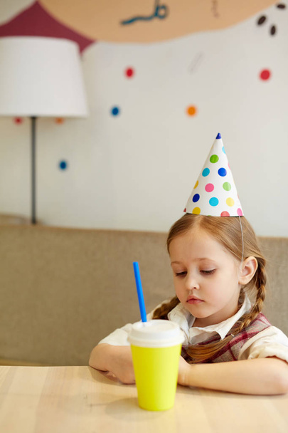 Набридла дитина зі склянкою содової, що сидить за столом
 - Фото, зображення