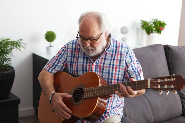 portrét starší muž s bílým vousem hrál na kytaru doma  - Fotografie, Obrázek