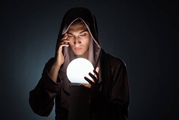 Молодой волшебник с хрустальным шаром в темной комнате - Фото, изображение
