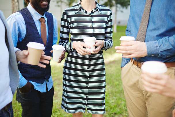 Des collègues joyeux passent de courtes pauses à l'extérieur : ils boivent du café dans des tasses en papier et bavardent animément, gros plan
 - Photo, image