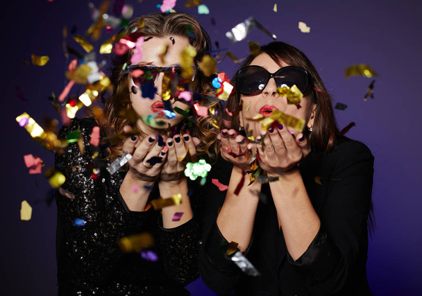 Attractive it girls wearing stylish clothes blowing colorful confetti while posing for photography in studio, waist-up portrait - Fotografie, Obrázek