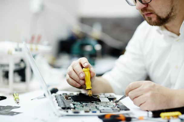 Closeup shot man working on assembling new circuit board using tweezers and screwdriver on table in maintenance shop - Фото, зображення
