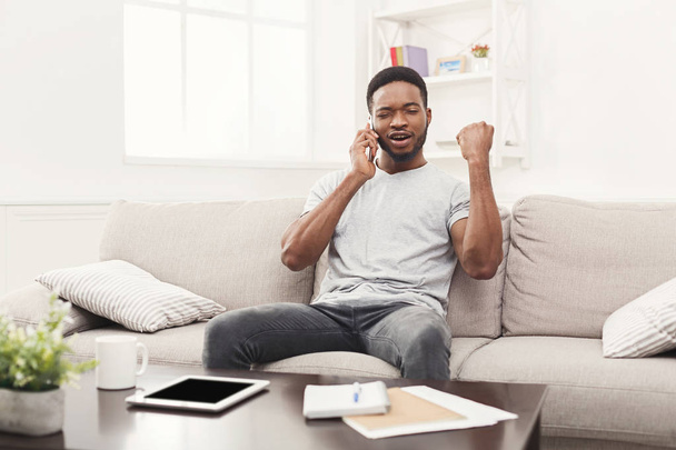Χαρούμενος νεαρός άνδρας μιλάει στο κινητό στο σπίτι - Φωτογραφία, εικόνα