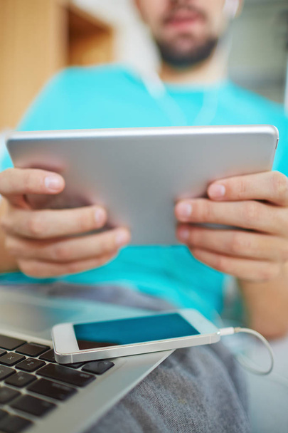 Close-up de empresário usando dispositivo portátil para trabalho ou lazer, smartphone e laptop de joelhos
 - Foto, Imagem