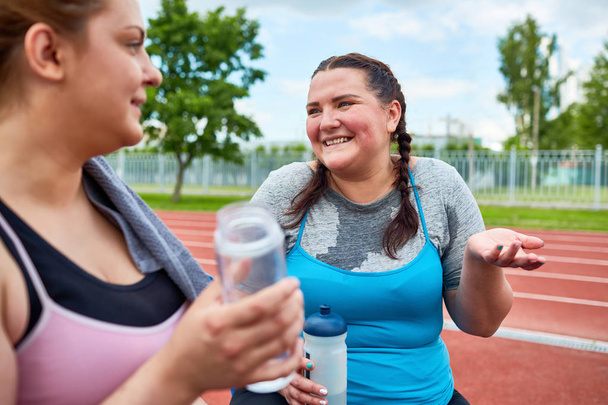 Mujeres jóvenes con agua conversando y refrescándonos en el estadio después de correr
 - Foto, imagen