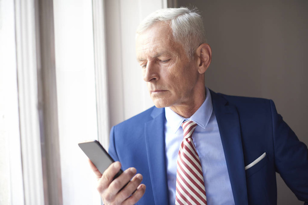 Senior businessman using mobile near window - Foto, Imagen