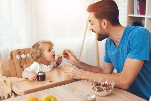 A man spends time with his son. The father of boy is engaged in raising child. Father feeds his son. The boy is having breakfast with his father. - Zdjęcie, obraz