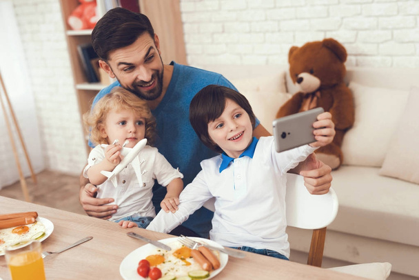 A man spends time with his sons. The father of two boys is engaged in raising children. Father feeds his son. Children have breakfast with their father. - Foto, afbeelding