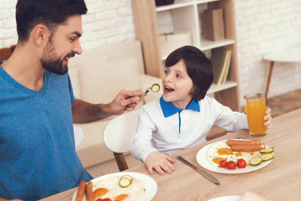 A man spends time with his son. The father of boy is engaged in raising child. Father feeds his son. The boy is having breakfast with his father. - Foto, Imagen