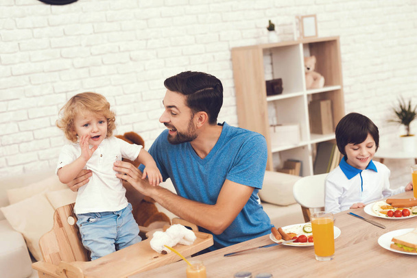 A man spends time with his sons. The father of two boys is engaged in raising children. Father feeds his son. Children have breakfast with their father. - Foto, Bild