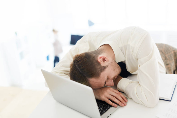 Gerente cansado durmiendo en el teclado portátil por su lugar de trabajo
 - Foto, Imagen