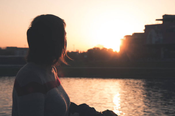 Молода дівчина дивиться на захід сонця над річкою
 - Фото, зображення