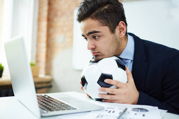 Молодий економіст з футбольним м'ячем дивиться футбольний матч перед ноутбуком
 - Фото, зображення