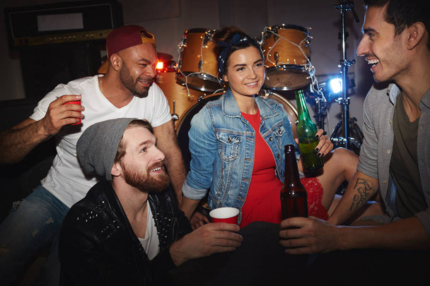 Jóvenes contemporáneos, tres hombres y una mujer, de fiesta en el club nocturno: beber cerveza y divertirse sentado en el escenario
 - Foto, imagen