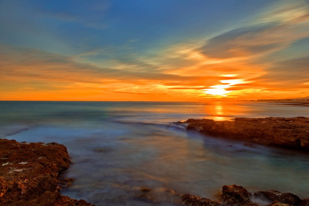 Tyyni meri hyvin pilvessä auringonlaskussa
 - Valokuva, kuva