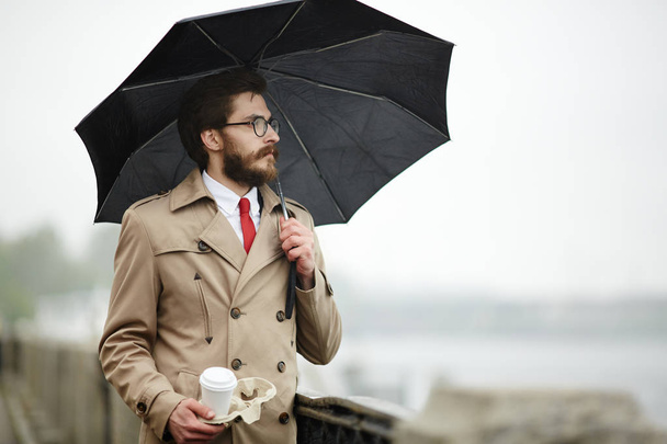 Elegant man with black umbrella and drink having walk in the city - Foto, afbeelding