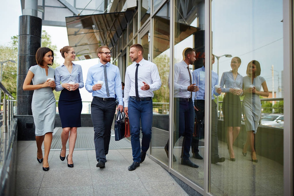 Группа молодых успешных бизнесменов покидает современное офисное здание и весело улыбается в чате по дороге
 - Фото, изображение