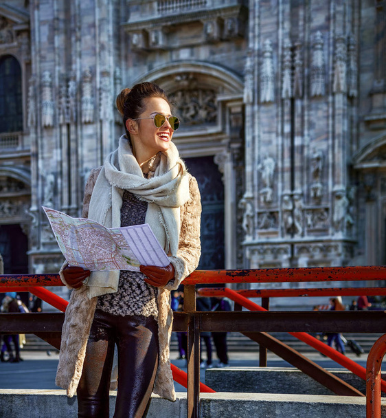 Retrato completo de mujer turista moderna sonriente en abrigo de piel y gafas de sol en Milán, Italia con mapa mirando a la distancia
 - Foto, Imagen