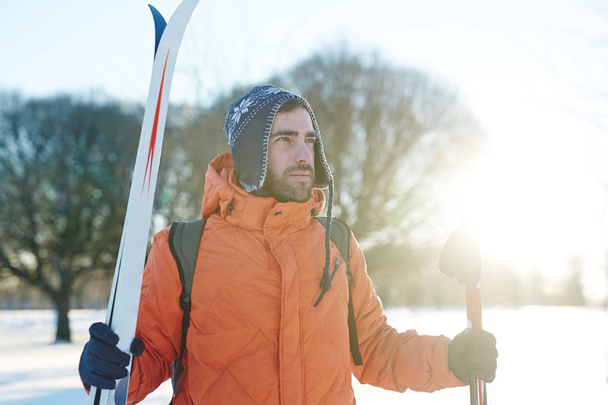 Aktiver Mann mit Skiausrüstung steht am Wintertag in ländlicher Umgebung - Foto, Bild