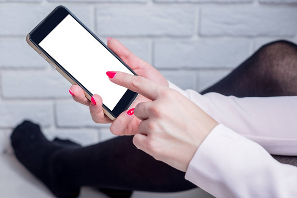 Το τηλέφωνο στο χέρι, δάχτυλο κλικ στην κενή οθόνη. Γυναίκα κάθεται στον τοίχο στο δωμάτιο και περιήγηση στο κινητό τηλέφωνο. Online ψώνια, προβολή μηνυμάτων, αποστολή μηνυμάτων. - Φωτογραφία, εικόνα
