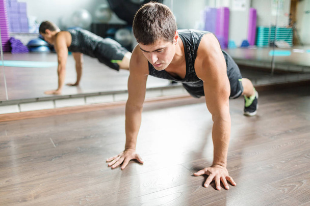 Портрет сильного мускулистого мужчины, отжимающегося во время тренировки в современной фитнес-студии рядом с зеркалом
 - Фото, изображение