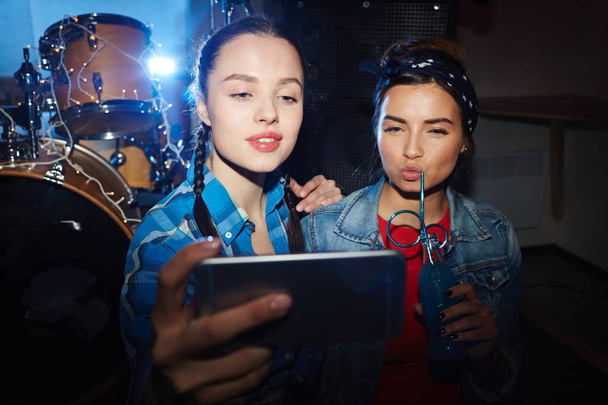 Portrait of two trendy teenage girls taking selfie in club, posing seductively - Photo, Image