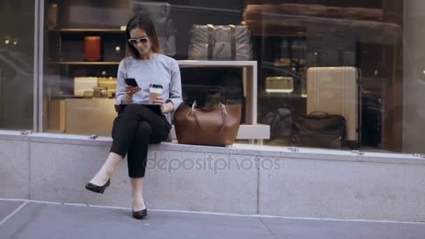 Mladá krásná obchodnice sedí u okna obchod, pití kávy a používání smartphone na přerušení. - Záběry, video