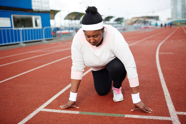 Giovane donna in sovrappeso in piedi dalla linea di partenza su pista pronto a correre
 - Foto, immagini