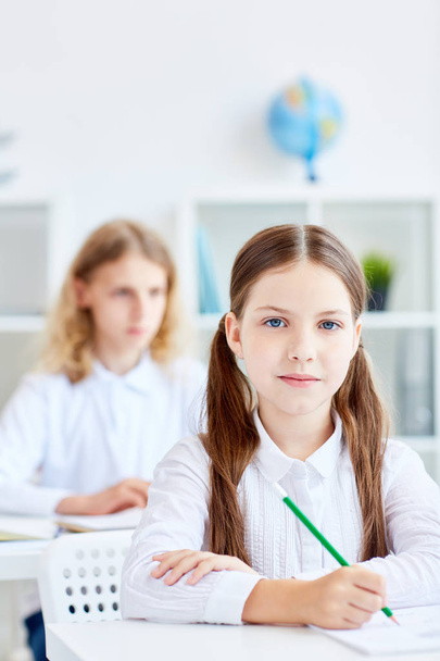 Chica con crayón y su compañero de clase en el fondo bosquejo en la lección
 - Foto, Imagen