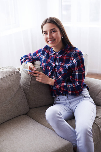 Девушка с телефоном на диване дома
 - Фото, изображение