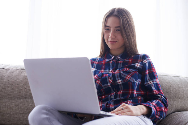 Dívka drží netbook na boky při sezení na pohovce  - Fotografie, Obrázek