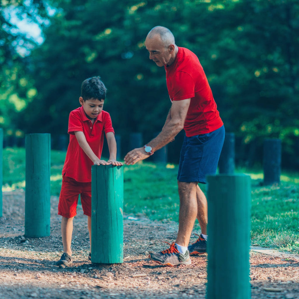 Opa en kleinzoon springen over houten kruipen in park - Foto, afbeelding