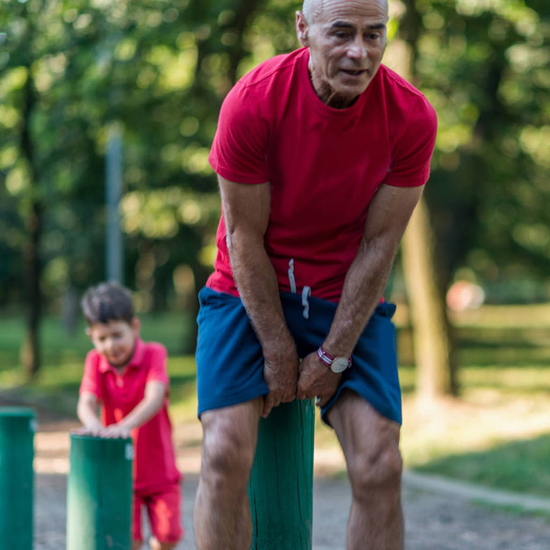 Grandfather and grandson jumping over wooden huddles in park - Foto, Bild