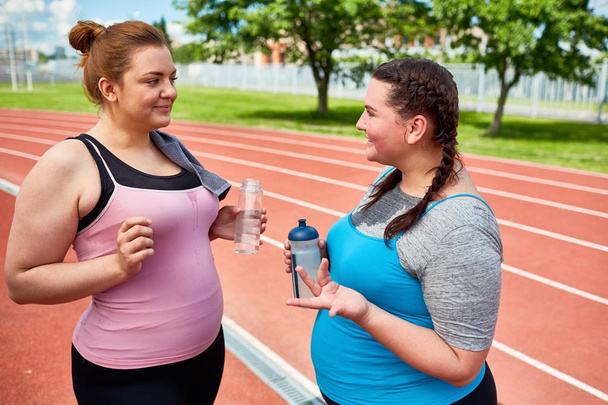 Conversa de duas fêmeas gordas em activewear água potável após o treinamento
 - Foto, Imagem